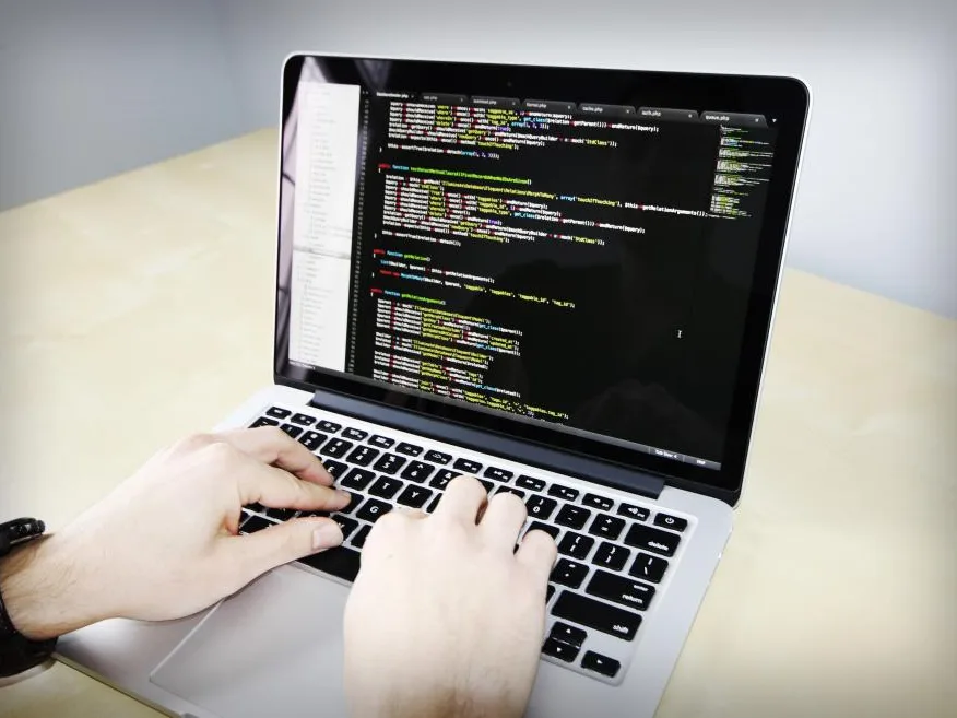 Manos escribiendo en un notebook con código en pantalla